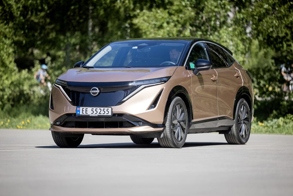 Gullgrå Nissan Ariya foran grrønne trær